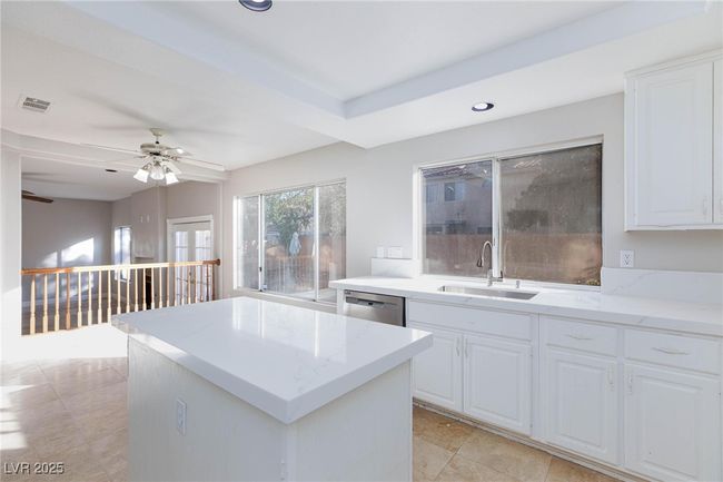 Kitchen featuring stainless steel dishwasher, visible vents, a center island, light stone counters, and a sink | Image 16