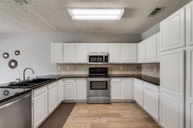 Kitchen featuring stainless steel appliances, white cabinetry, a textured ceiling, and backsplash | Image 10