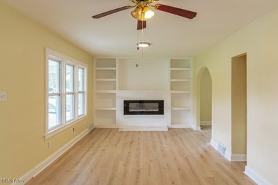 Unfurnished living room with ceiling fan, built in features, and light hardwood / wood-style floors | Image 2