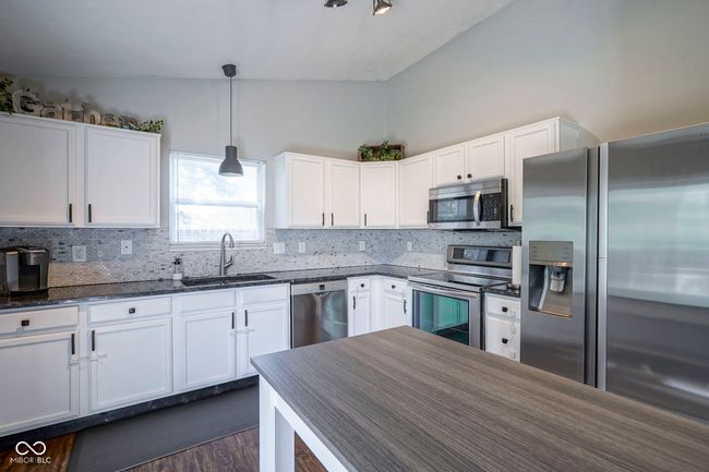 kitchen featuring white cabinetry, tasteful backsplash, a sink, stainless steel appliances, and hanging light fixtures | Image 13