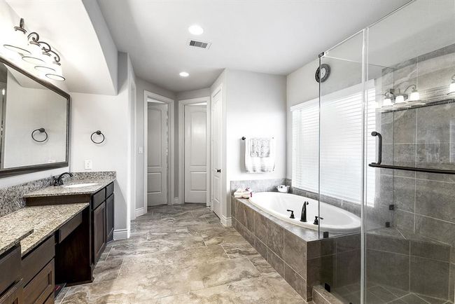The primary en suite bathroom offers a spa-like experience with an abundance of space! It features two separate sinks with a prep vanity in between, providing plenty of room for personal use. A luxurious garden bathtub invites relaxation, while the glass-tiled shower includes a built-in bench for added comfort. The large wardrobe closet offers ample storage. | Image 22