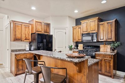 Kitchen featuring light stone counters, black appliances, a center island, and a kitchen bar | Image 3