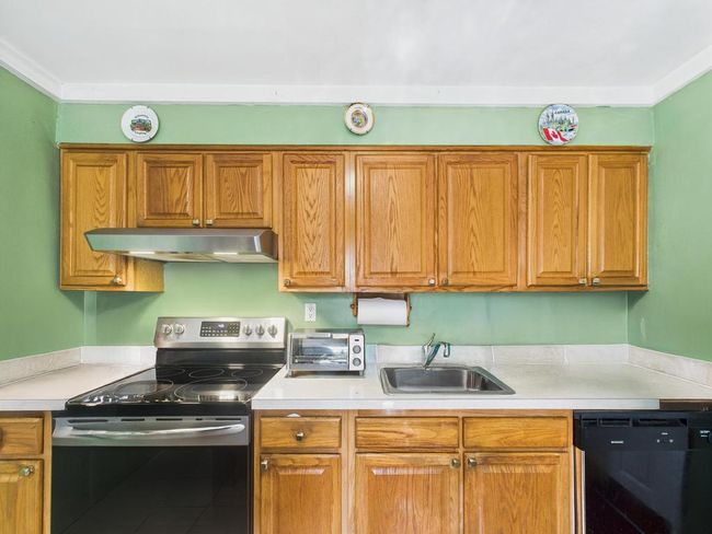 Kitchen with stainless steel electric range oven, range hood, dishwasher, light countertops, and brown cabinets | Image 6