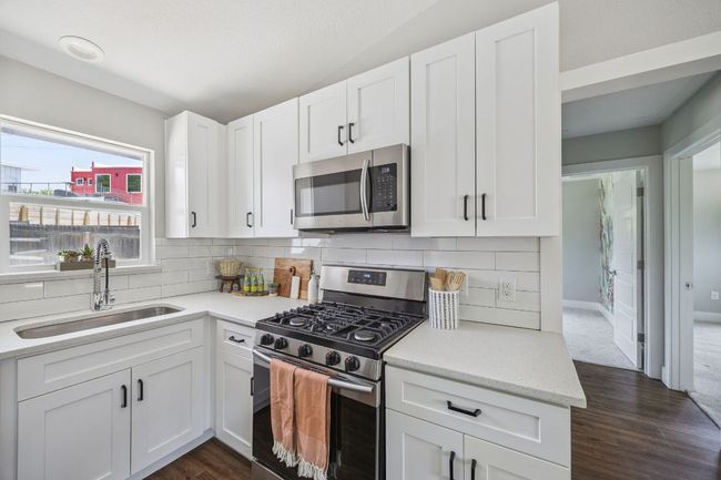 Kitchen featuring appliances with stainless steel finishes, dark wood-style floors, backsplash, and white cabinetry | Image 15