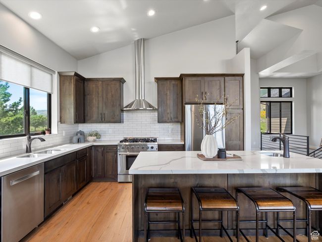 Kitchen with appliances with stainless steel finishes, lofted ceiling, a sink, wall chimney exhaust hood, and light stone countertops | Image 16