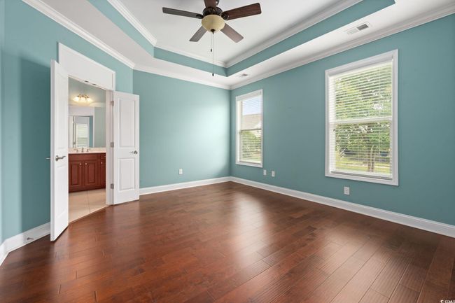 Unfurnished bedroom with a tray ceiling, crown molding, visible vents, baseboards, and dark wood finished floors | Image 18