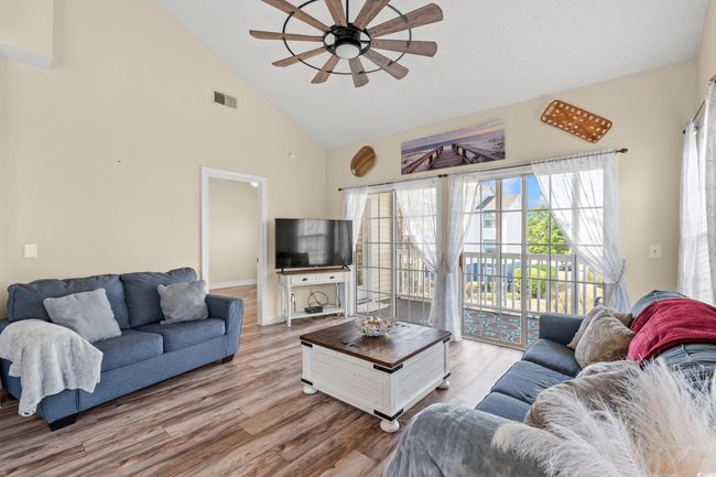 Living room with high vaulted ceiling, visible vents, baseboards, ceiling fan, and wood finished floors | Image 5