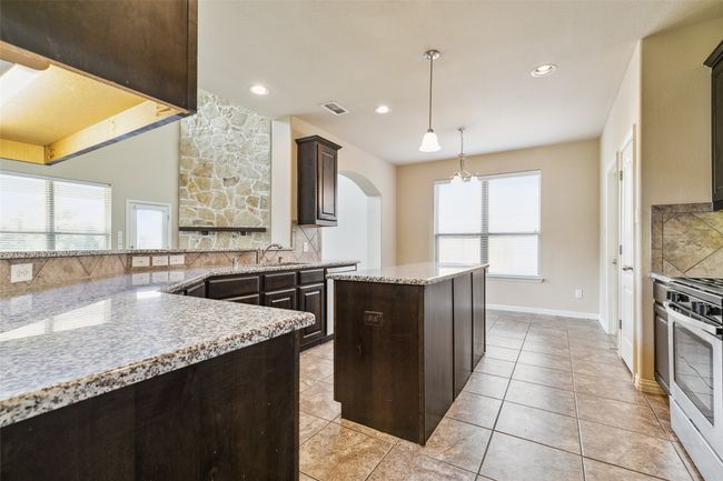 Kitchen featuring stainless steel stove, arched walkways, decorative backsplash, dark brown cabinets, and recessed lighting | Image 10