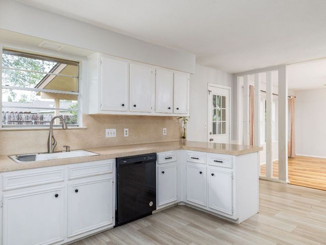 Kitchen with black dishwasher, light wood-style flooring, white cabinets, and backsplash | Image 9