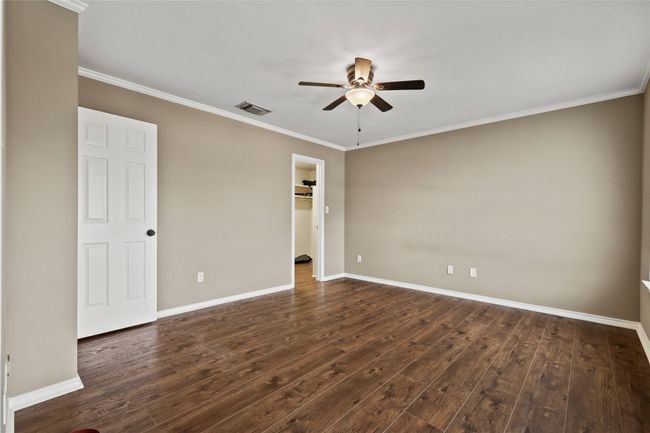 Unfurnished bedroom featuring dark wood-type flooring, crown molding, a spacious closet, ceiling fan, and a closet | Image 29