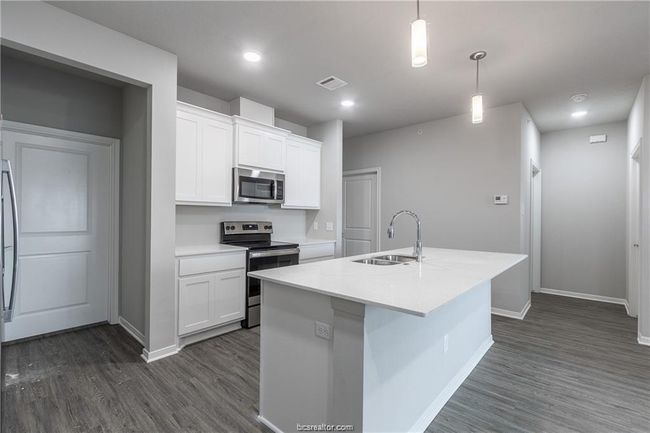 Kitchen with decorative light fixtures, stainless steel appliances, an island with sink, white cabinetry, and sink | Image 10