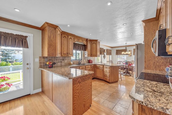 Kitchen featuring a peninsula, appliances with stainless steel finishes, a sink, a chandelier, and backsplash | Image 9