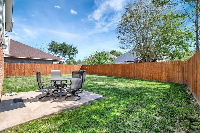 This backyard features a spacious, grassy lawn with a wooden privacy fence. A small patio area hosts a modern outdoor dining set, perfect for relaxation or entertaining under clear skies. | Image 42
