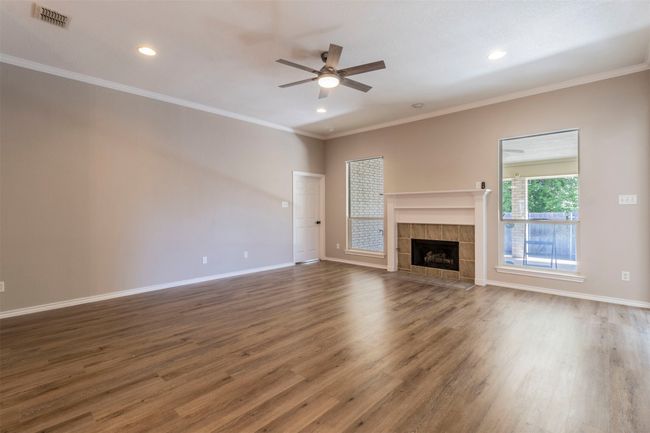 Unfurnished living room with crown molding, wood finished floors, ceiling fan, a fireplace, and baseboards | Image 4