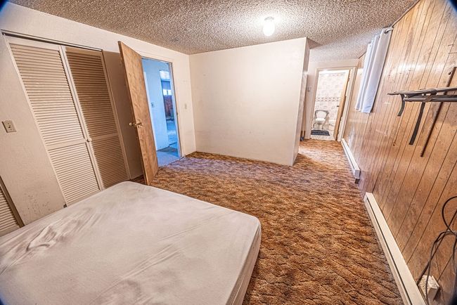 Unfurnished bedroom with carpet flooring, wooden walls, a textured ceiling, a baseboard radiator, and a closet | Image 38