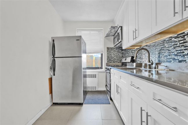 Kitchen with appliances with stainless steel finishes, radiator, tasteful backsplash, white cabinets, and dark countertops | Image 8