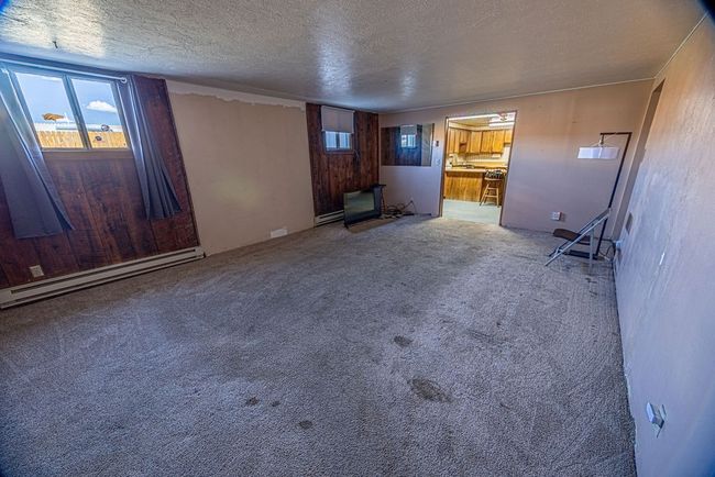 Unfurnished living room with carpet floors, wood walls, a textured ceiling, and baseboard heating | Image 40