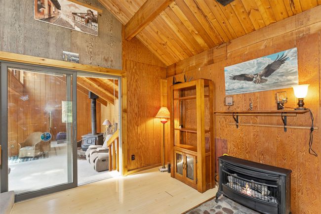 Living room with a wood stove, wood finished floors, wood walls, wooden ceiling with exposed beams, and high vaulted ceiling | Image 25