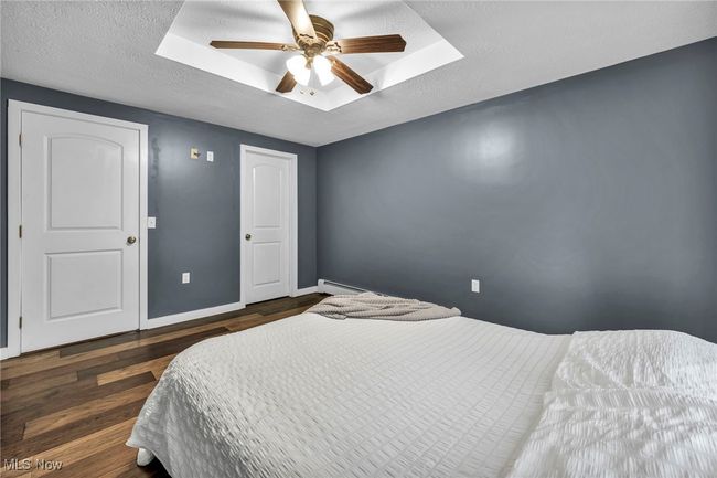 Bedroom featuring a baseboard heating unit, wood floors, ceiling fan, and a textured ceiling | Image 23