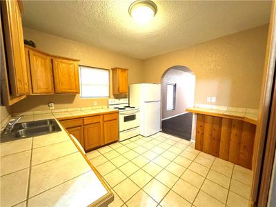 Kitchen featuring a textured ceiling, tile countertops, sink, and white appliances | Image 3