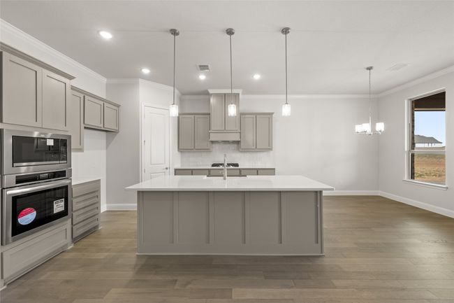 Kitchen featuring gray cabinets, stainless steel oven, built in microwave, backsplash, and light countertops | Image 4