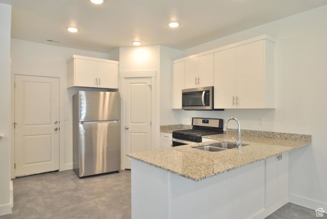 Kitchen with appliances with stainless steel finishes, a peninsula, light stone counters, white cabinetry, and recessed lighting | Image 4