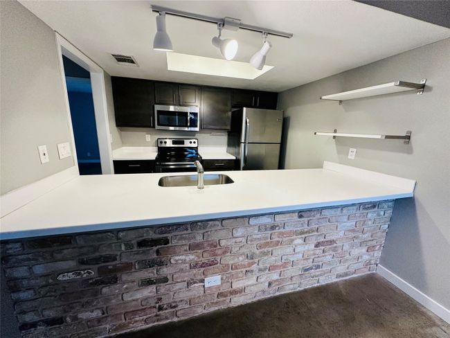 Kitchen with a peninsula, appliances with stainless steel finishes, dark cabinetry, and light countertops | Image 5