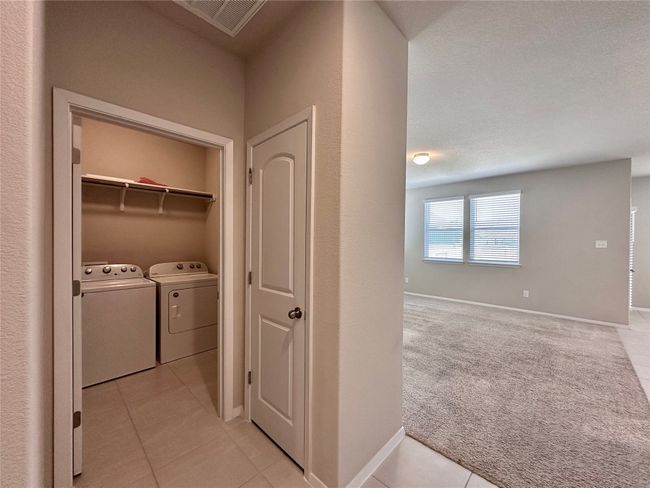 Laundry area featuring independent washer and dryer, light tile patterned flooring, and light colored carpet | Image 18