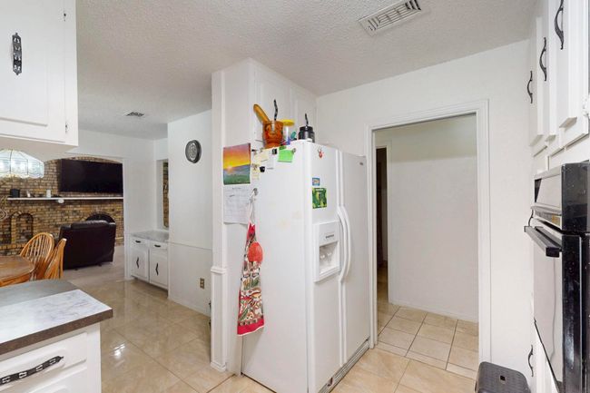 Kitchen featuring white cabinetry, light tile patterned floors, black oven, visible vents, and white fridge with ice dispenser | Image 15