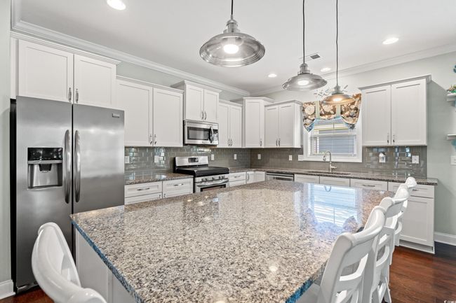Kitchen featuring stainless steel appliances, crown molding, white cabinetry, a center island, and light stone countertops | Image 11