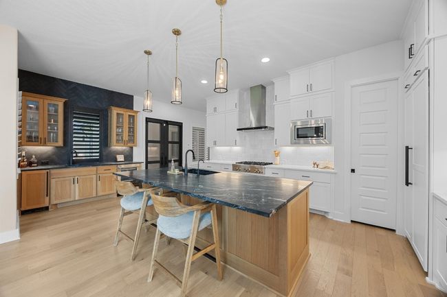 Kitchen with a kitchen island with sink, glass insert cabinets, light wood-style floors, a kitchen breakfast bar, and recessed lighting | Image 4