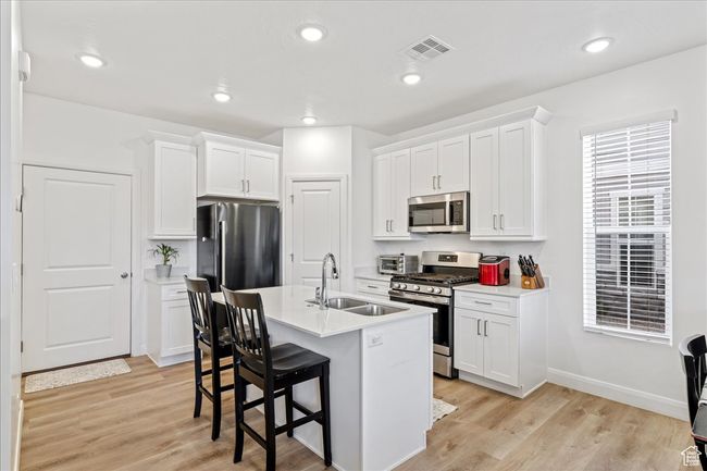 Kitchen with appliances with stainless steel finishes, a kitchen bar, white cabinetry, light countertops, and recessed lighting | Image 8