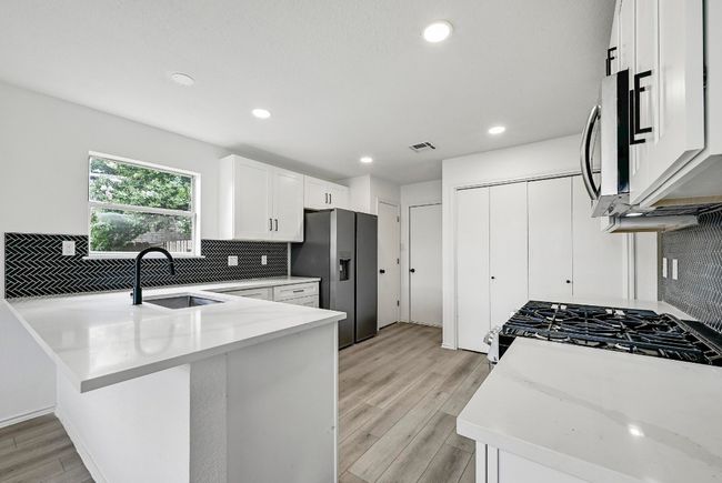 Kitchen with appliances with stainless steel finishes, backsplash, a peninsula, white cabinets, and recessed lighting | Image 11