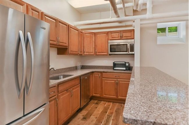 Kitchen featuring stainless steel appliances, a sink, light wood-type flooring, light stone counters, and brown cabinetry | Image 29