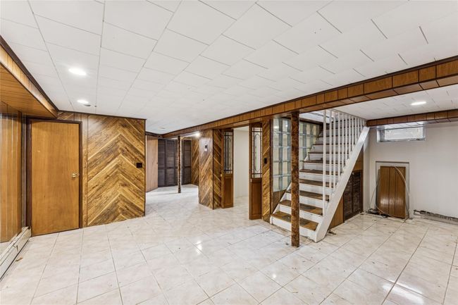 Basement with baseboard heating, wood walls, and stairway | Image 14