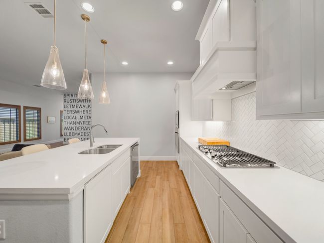 Kitchen with light wood-type flooring, recessed lighting, a kitchen island with sink, light countertops, and white cabinets | Image 9