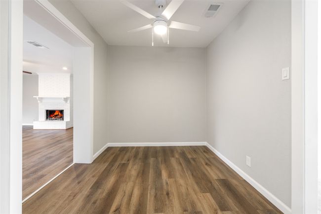 Unfurnished room featuring a ceiling fan, wood finished floors, and a brick fireplace | Image 5