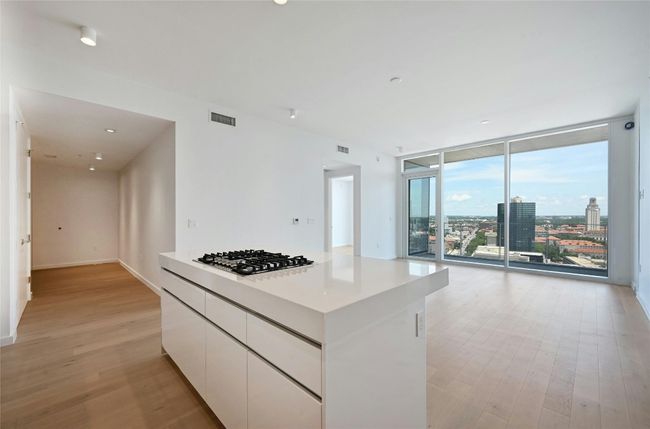 Sophisticated open-concept kitchen featuring sleek Bosch appliances, integrated wood-paneled cabinetry, and a glossy white island ideal for casual dining or entertaining—all seamlessly connected to the main living space with clean, modern lines. | Image 6
