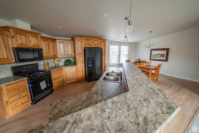 Kitchen with tasteful backsplash, light wood finished floors, a sink, and black appliances | Image 27