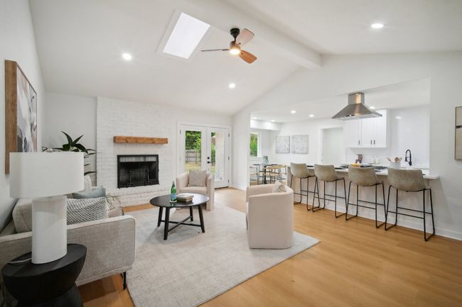 Living room with light wood finished floors, recessed lighting, lofted ceiling with skylight, and a brick fireplace | Image 6