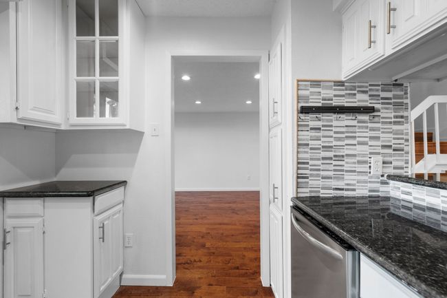 Kitchen featuring tasteful backsplash, dark wood-style flooring, dark stone countertops, white cabinetry, and stainless steel dishwasher | Image 14