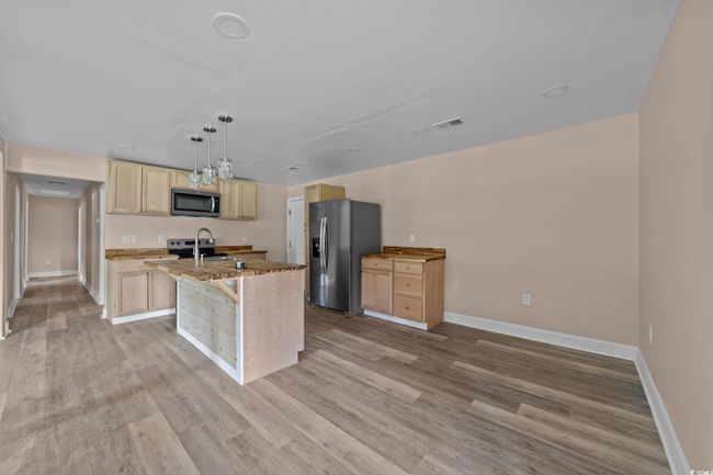 Kitchen featuring light brown cabinetry, light wood finished floors, appliances with stainless steel finishes, and a kitchen island with sink | Image 22