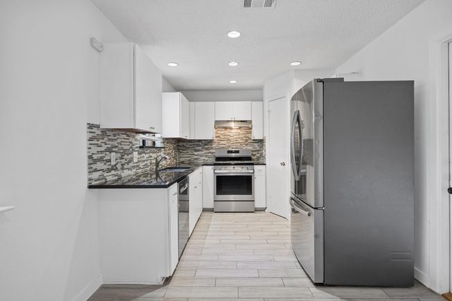 Kitchen with a sink, appliances with stainless steel finishes, white cabinetry, backsplash, and under cabinet range hood | Image 10