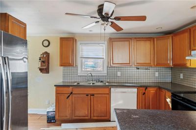 Kitchen featuring white dishwasher, sink, backsplash, and stainless steel refrigerator | Image 2