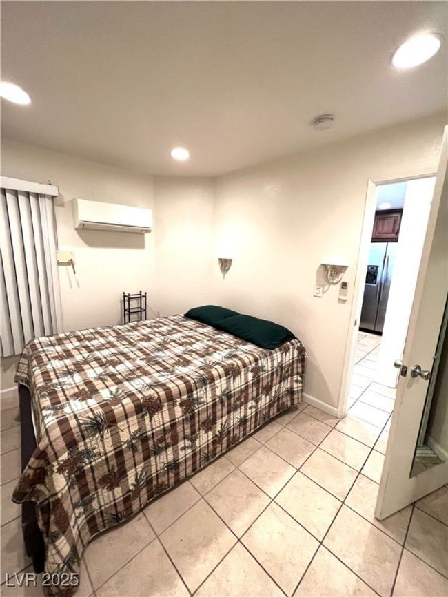 Bedroom featuring light tile patterned flooring, stainless steel refrigerator with ice dispenser, baseboards, an AC wall unit, and recessed lighting | Image 24
