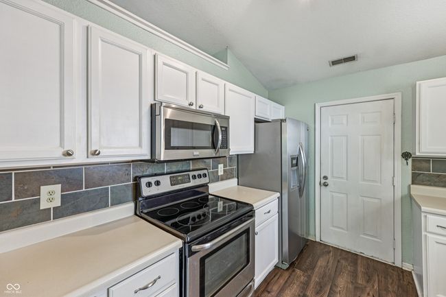 kitchen featuring stainless steel appliances, lofted ceiling, white cabinets, decorative backsplash, and dark wood-style floors | Image 13