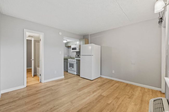 Kitchen featuring white appliances, light wood-type flooring, baseboards, a textured ceiling, and a sink | Image 8