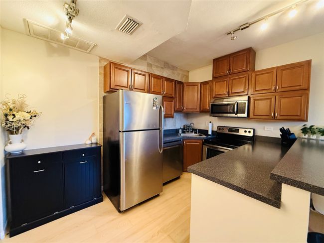 Kitchen with dark countertops, appliances with stainless steel finishes, brown cabinets, a peninsula, and a sink | Image 10