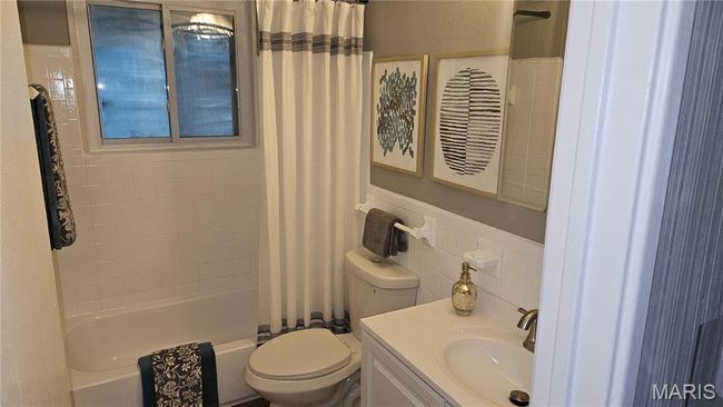 Bathroom with tile walls, shower / bath combo with shower curtain, vanity, and decorative backsplash | Image 12