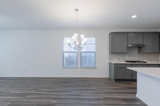 Kitchen featuring a notable chandelier, gray cabinetry, under cabinet range hood, dark wood finished floors, and light countertops | Image 12
